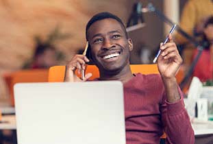 Happy young man on phone sitting behind laptop.